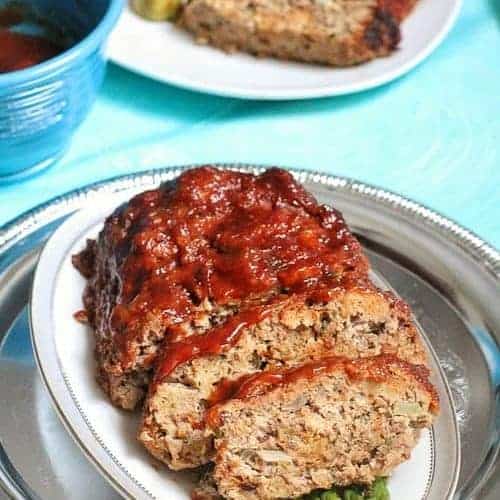 A slow cooker meatloaf cut into slices on a white oval platter 