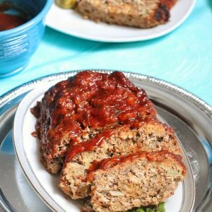 A slow cooker meatloaf cut into slices over asparagus on a white oval platter