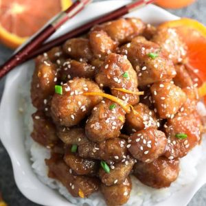 Orange chicken over a bed of white rice in a white bowl with chopsticks