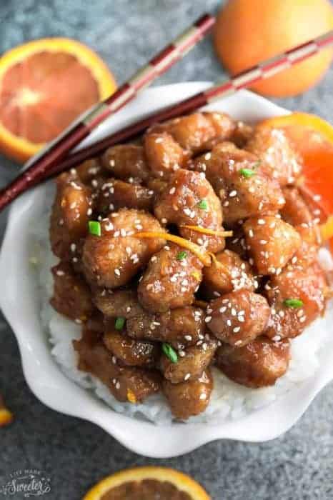 Orange chicken over a bed of white rice in a white bowl with chopsticks