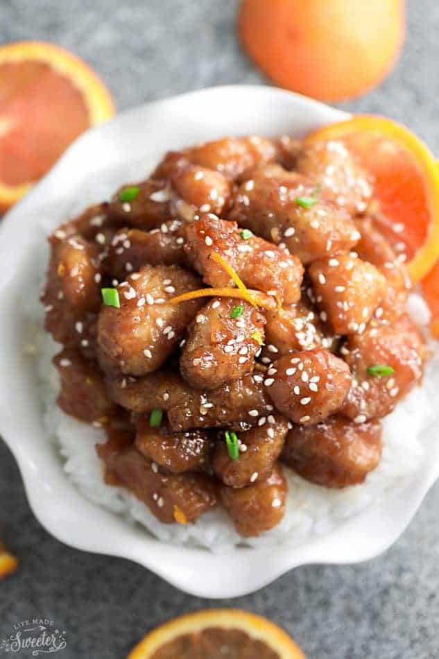 Instant pot Orange Chicken on a bed of white rice in a small white bowl surrounded by sliced oranges.
