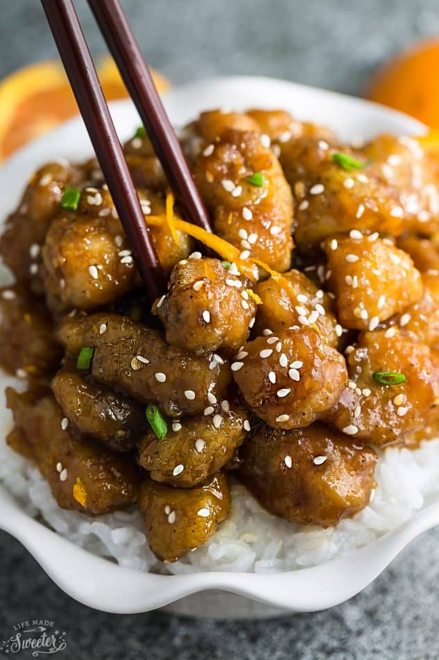 Slow Cooker Orange Chicken covered in sesame seeds and green onions on a bed of white rice in a small white bowl.