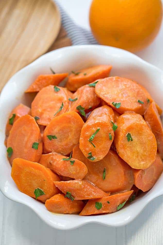 Top view of orange glazed slow cooker carrots in white bowl.