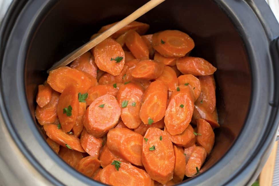 Slow cooker carrots with wooden spoon in black Crockpot. 