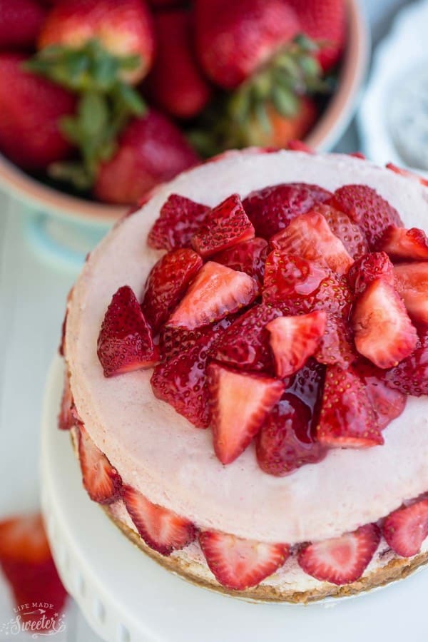 Close-up of Keto Strawberry Cheesecake topped with fresh strawberries on a white cake pedestal