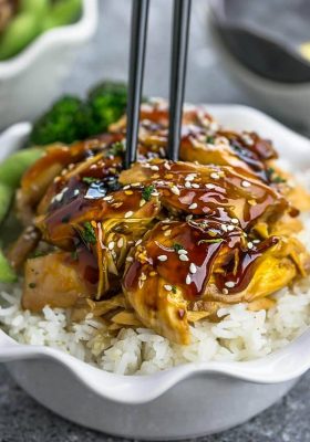 Slow Cooker Teriyaki Chicken coated in a homemade sweet and savory Teriyaki sauce on a bed of white rice in a white bowl with chopsticks.