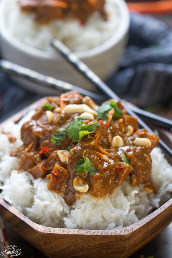 Close up image of slow cooker peanut chicken in wooden bowl with two dark chopsticks. 