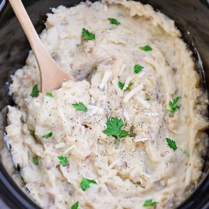Top view of slow cooker mashed potatoes in a 6 quart slow cooker with a wooden spoon