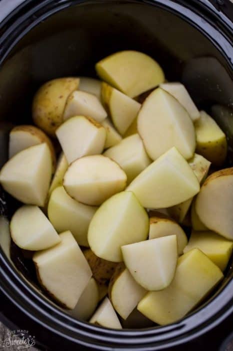 Top view of cut Russet potatoes and garlic in a 6 quart slow cooker