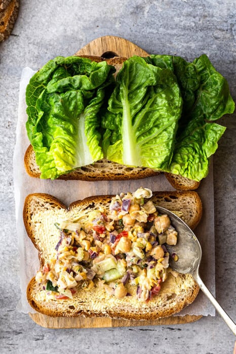 Building a chickpea salad sandwich on a piece of gluten free bread with lettuce