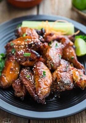 A pile of glazed spicy chicken wings on a black plate