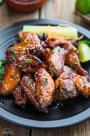 A pile of glazed spicy chicken wings on a black plate