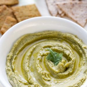 A bowl of homemade spinach hummus in a white bowl with parlsey