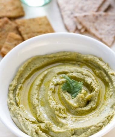 A bowl of homemade spinach hummus in a white bowl with parlsey