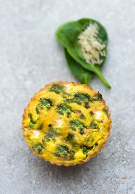 Top view of one spinach egg muffin with cheese on a grey background