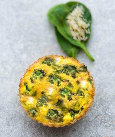 A Spinach and Cheese Egg Muffin Next to Two Spinach Leaves and Garlic Powder on a Countertop