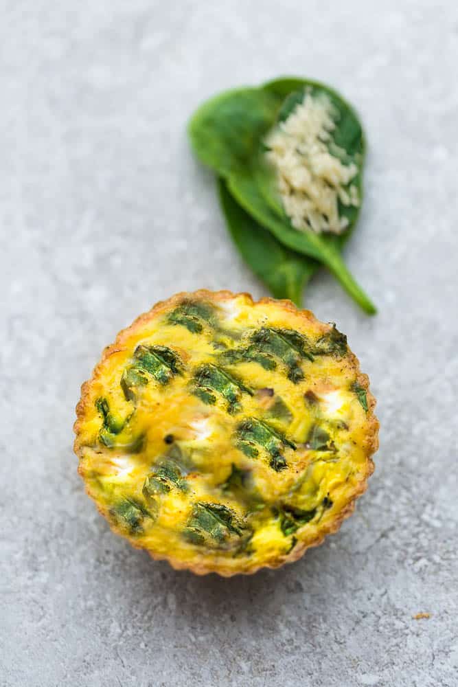 A Spinach and Cheese Egg Muffin Next to Two Spinach Leaves and Garlic Powder on a Countertop