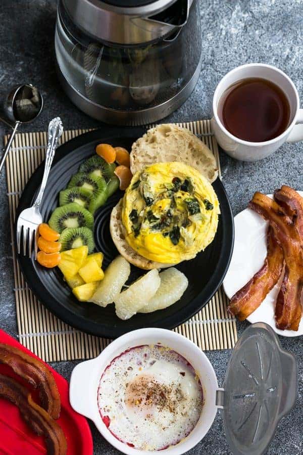 Overhead view of Spinach and Egg Breakfast Sandwich on a plate with fresh fruit next to coffee and bacon