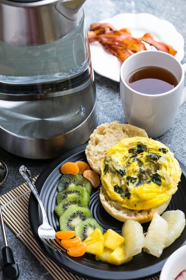 Overhead view of Spinach and Egg Breakfast Sandwich on a plate with fresh fruit next to coffee and bacon