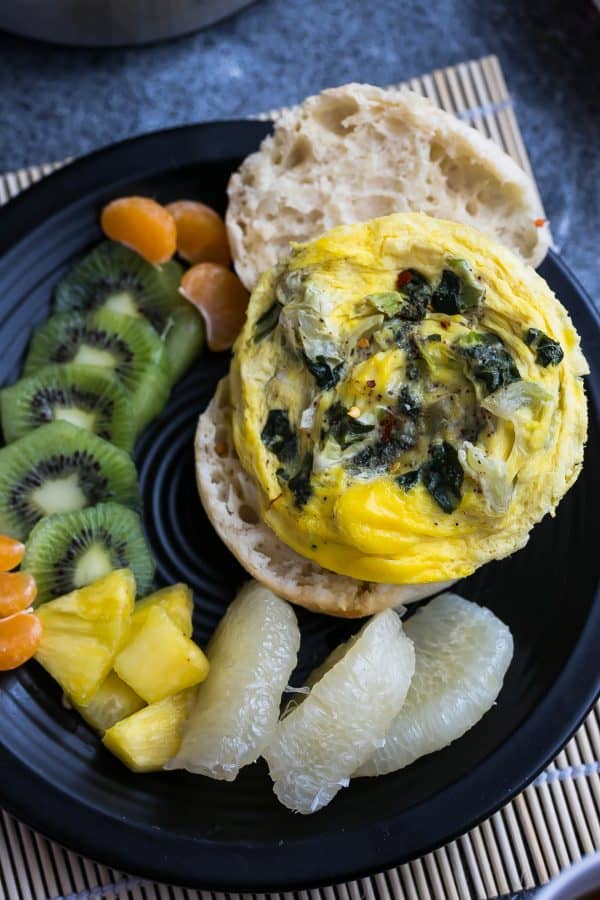 Overhead view of Spinach and Egg Breakfast Sandwich on a plate with fresh fruit