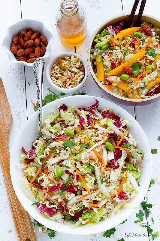 Overhead view of two bowls of Sriracha Asian Crunchy Ramen Noodle Salad surrounded by ingredients and a jar of dressing