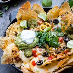 Overhead view of Sriracha Honey Chicken Nachos in a cast-iron skillet topped with garnishes