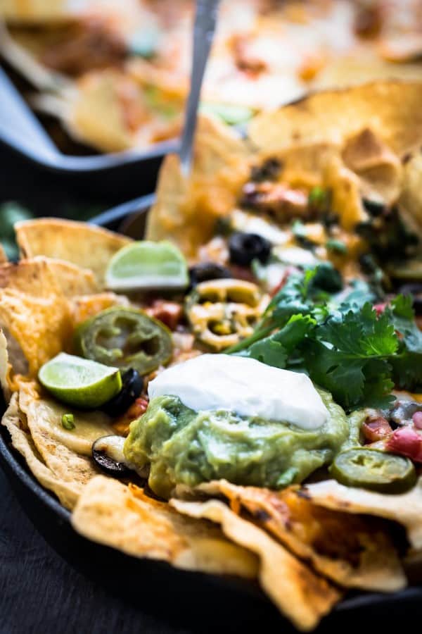 Close-up of Sriracha Honey Chicken Nachos in a skillet with garnishes