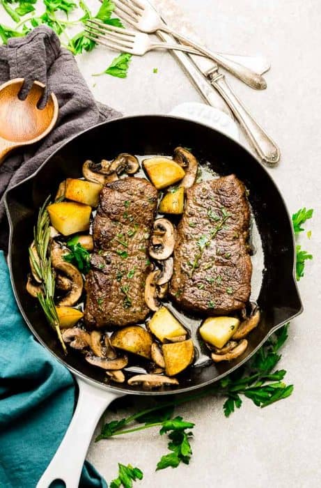 Top view of steak and Potatoes in a white cast iron pan with rosemary and spoon