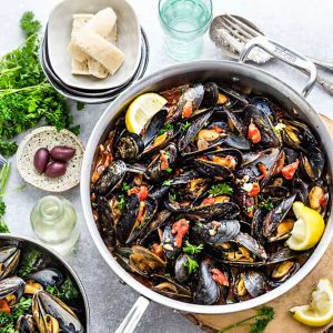 Top view of a serving bowl of Mediterranean Mussels with lemon wedges and olives