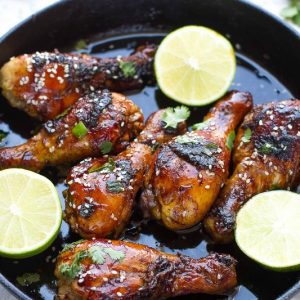 Sticky Honey Sriracha Chicken drumsticks in a skillet with lime halves