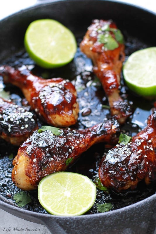 Sticky Honey Sriracha Chicken Drumsticks in a skillet with lime halves