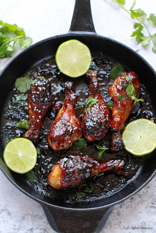 Sticky Honey Sriracha Chicken drumsticks in a skillet with lime halves