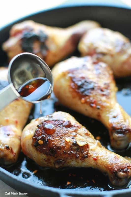Sticky Honey Sriracha sauce being poured over Chicken drumsticks in a skillet