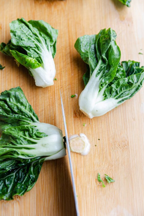 Three bok choy bunches on a wooden cutting board with a knife