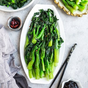 Flat lay of stir fried Chinese broccoli with chili flakes on a white oval plate with black chopsticks