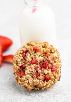 One Strawberry Cookie on a grey background leaning against a milk glass