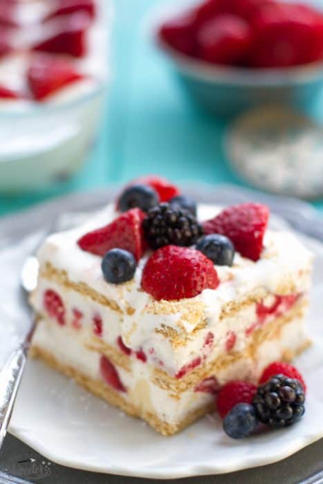 Top view of one slice of icebox cake on a white plate with a fork and mixed berries