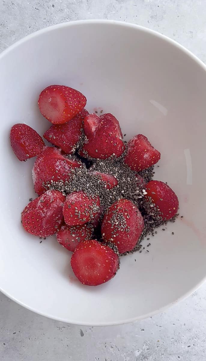 Frozen strawberries, chia seeds and maple syrup in a white bowl