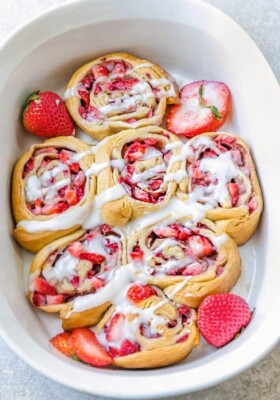 A batch of 7 strawberry cinnamon rolls with glaze in a white casserole pan