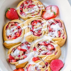 A batch of 7 strawberry cinnamon rolls with glaze in a white casserole pan