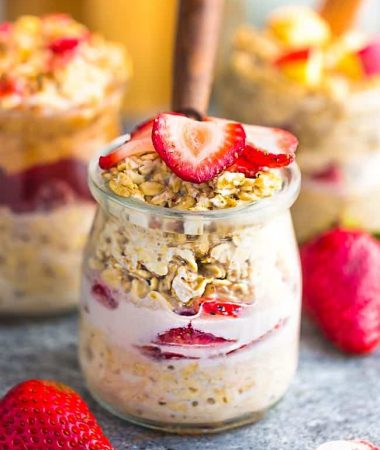 Side view strawberry overnight oats with strawberries with a spoon on a grey background with other overnight oats flavors in the background
