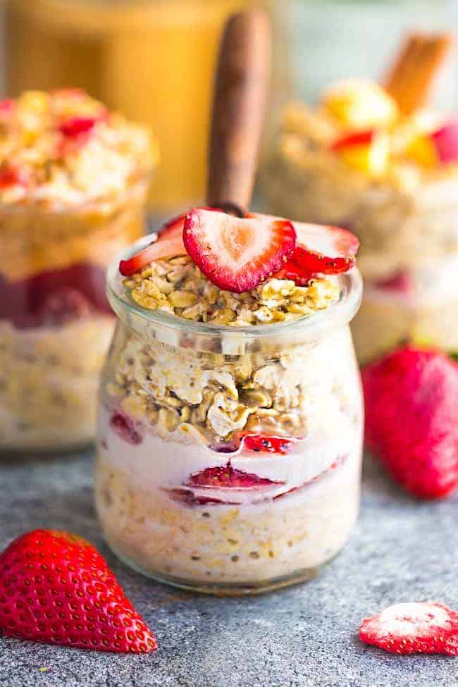 Side view strawberry overnight oats with strawberries with a spoon on a grey background with other overnight oats flavors in the background
