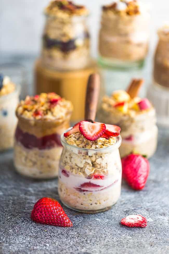 Side view strawberry overnight oats with strawberries with a spoon on a grey background with other overnight oats flavors in the background