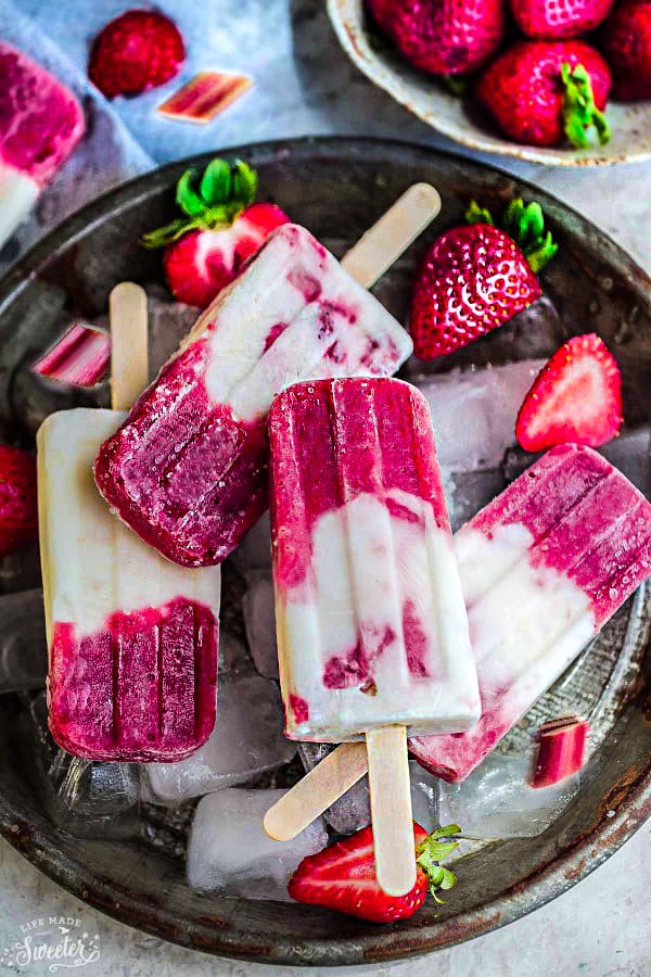 Top view of strawberry rhubarb Popsicles with fresh strawberries and ice.