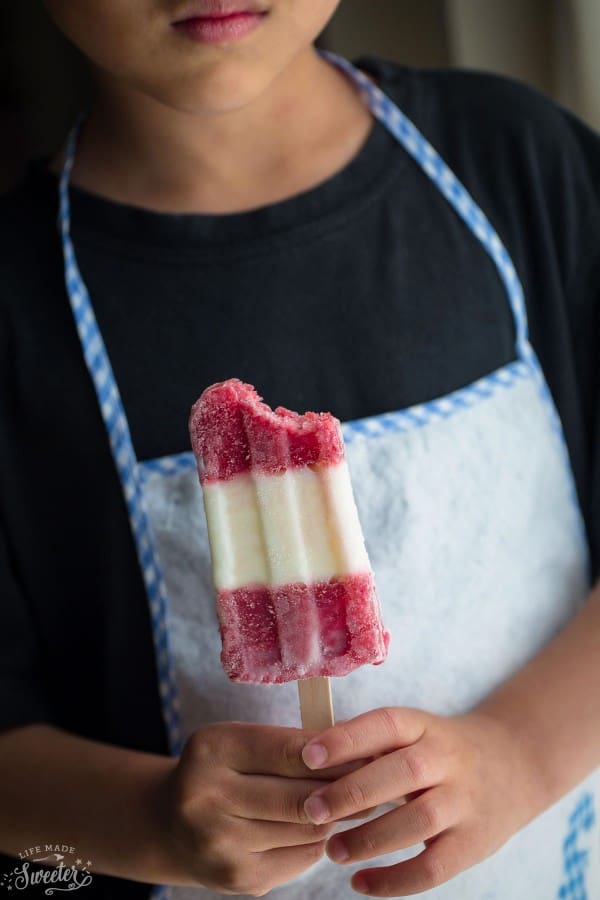 Strawberry rhubarb Popsicle being held in hands by child with white apron.