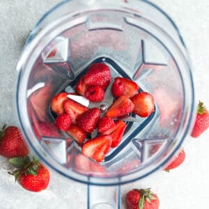 Top view of fresh strawberries and rasperries in a Vitamix blender on a grey background