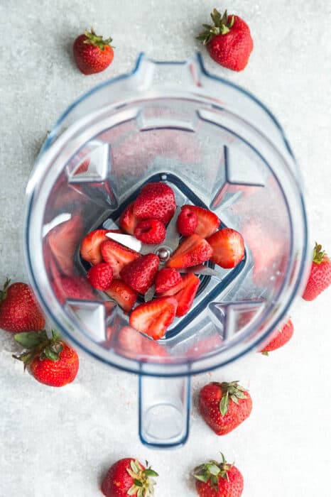 Top view of fresh strawberries and rasperries in a Vitamix blender on a grey background