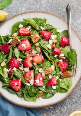 Top view of keto strawberry spinach salad in a white bowl on a grey background