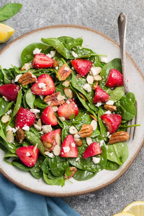 Top view of keto strawberry spinach salad in a white bowl on a grey background
