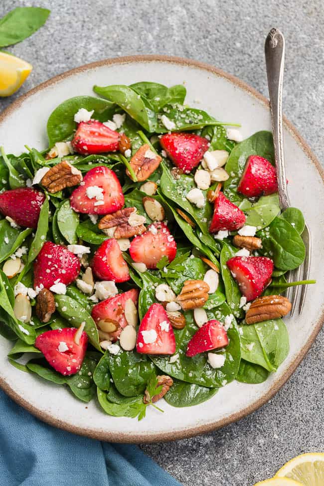 Top view of keto strawberry spinach salad in a white bowl on a grey background
